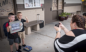 Two young students hold first day of school sign while staff takes a photo